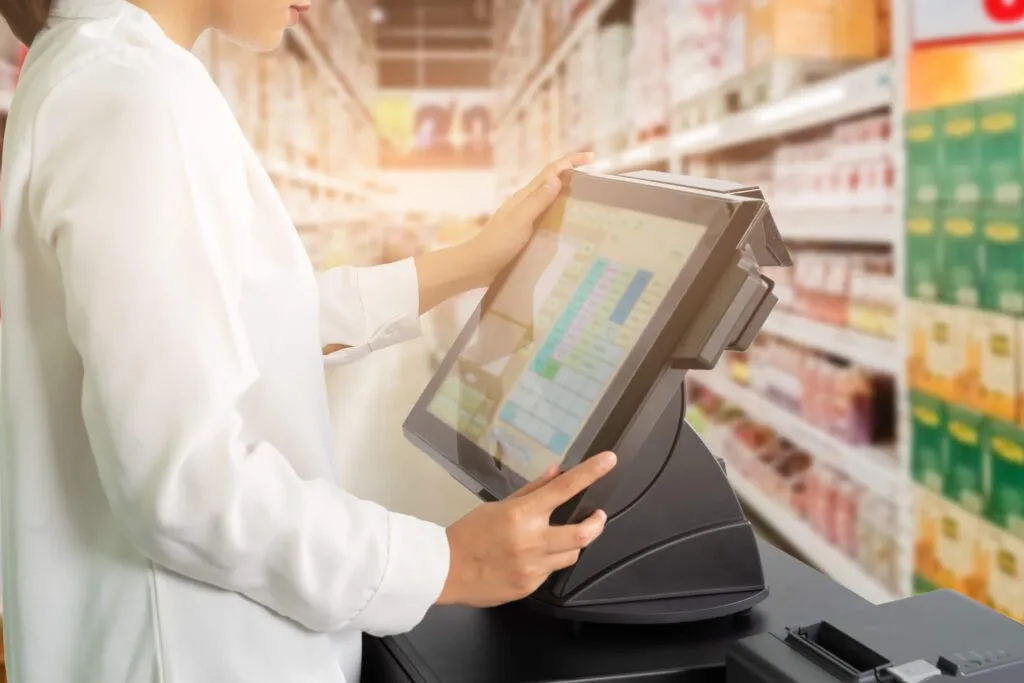 Cropped shot of female cashier staff standing and working with POS or point of sale machine at counter in supermarket