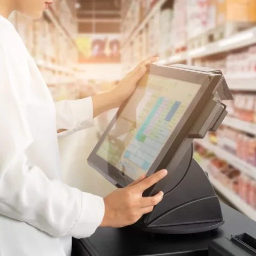 Cropped shot of female cashier staff standing and working with POS or point of sale machine at counter in supermarket